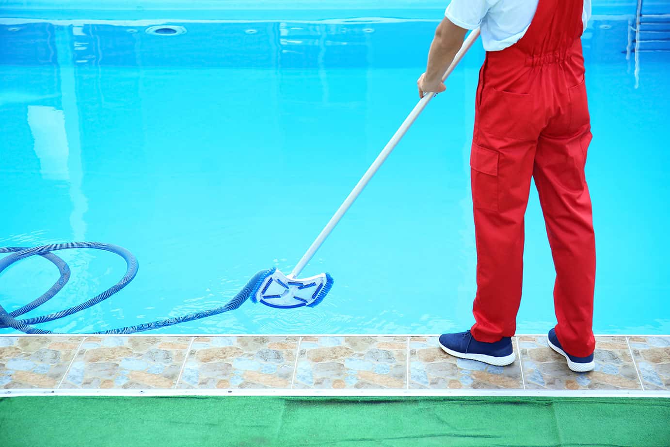 Male worker cleaning outdoor pool with underwater vacuum